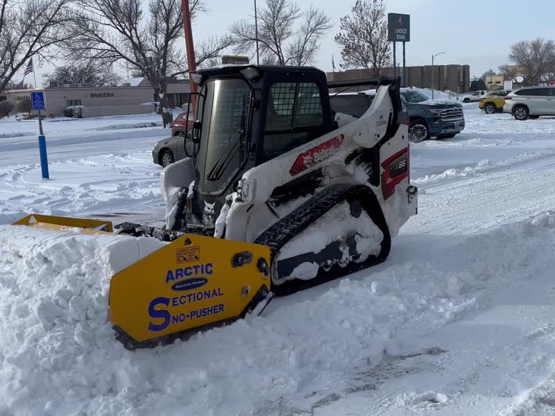 Stormworthy track loader pushing a full box of snow across a commercial parking lot in Bismarck, ND