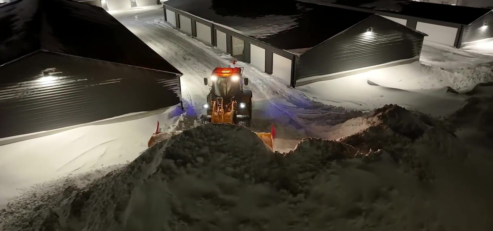 Stormworthy machine stacking snow into a pile on a commercial lot at night