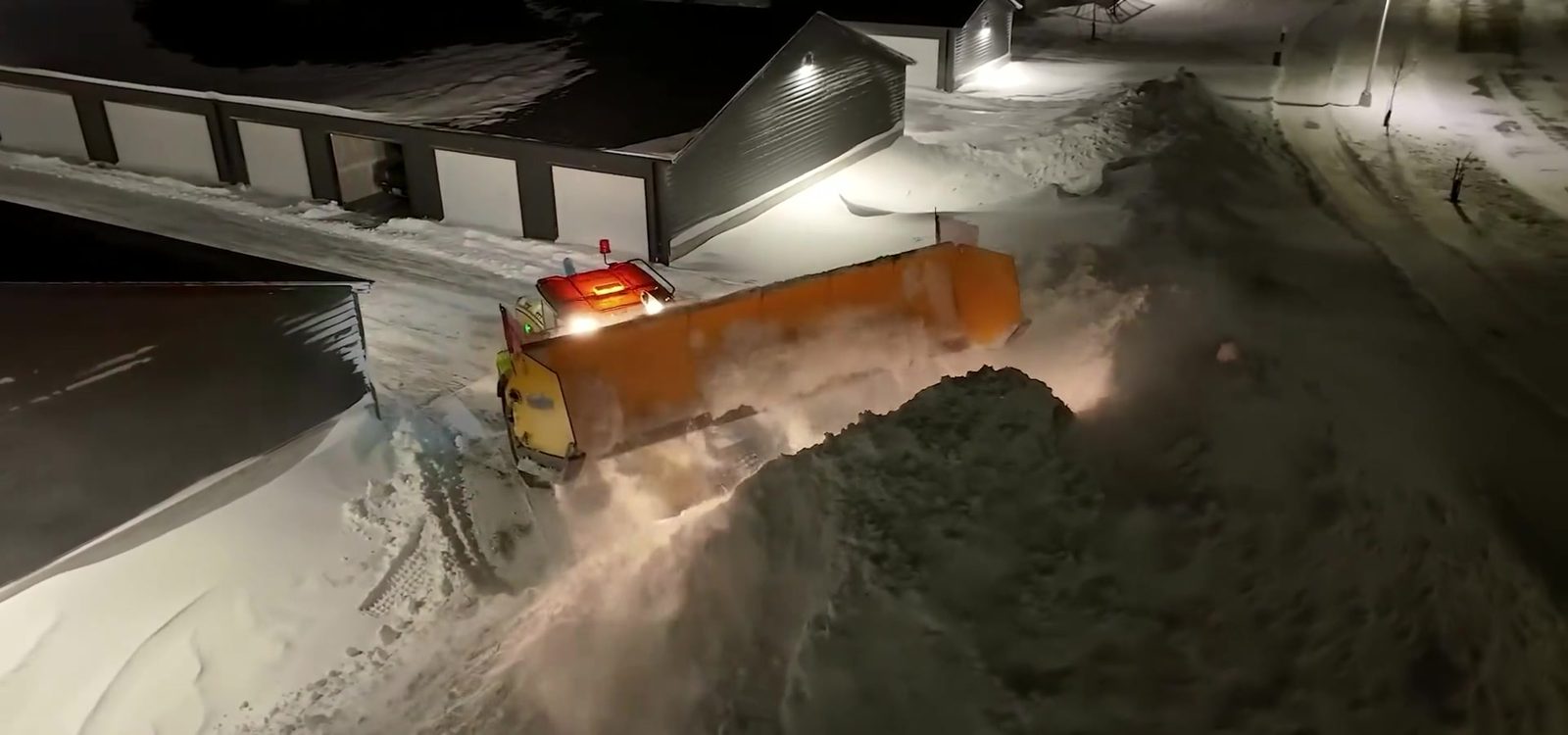 Sectional pusher moving a full box of snow across a commercial lot at night