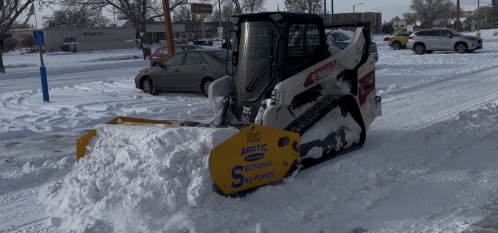 Stormworthy skid steer with an Arctic sectional pusher clearing a commercial lot in Bismarck, ND