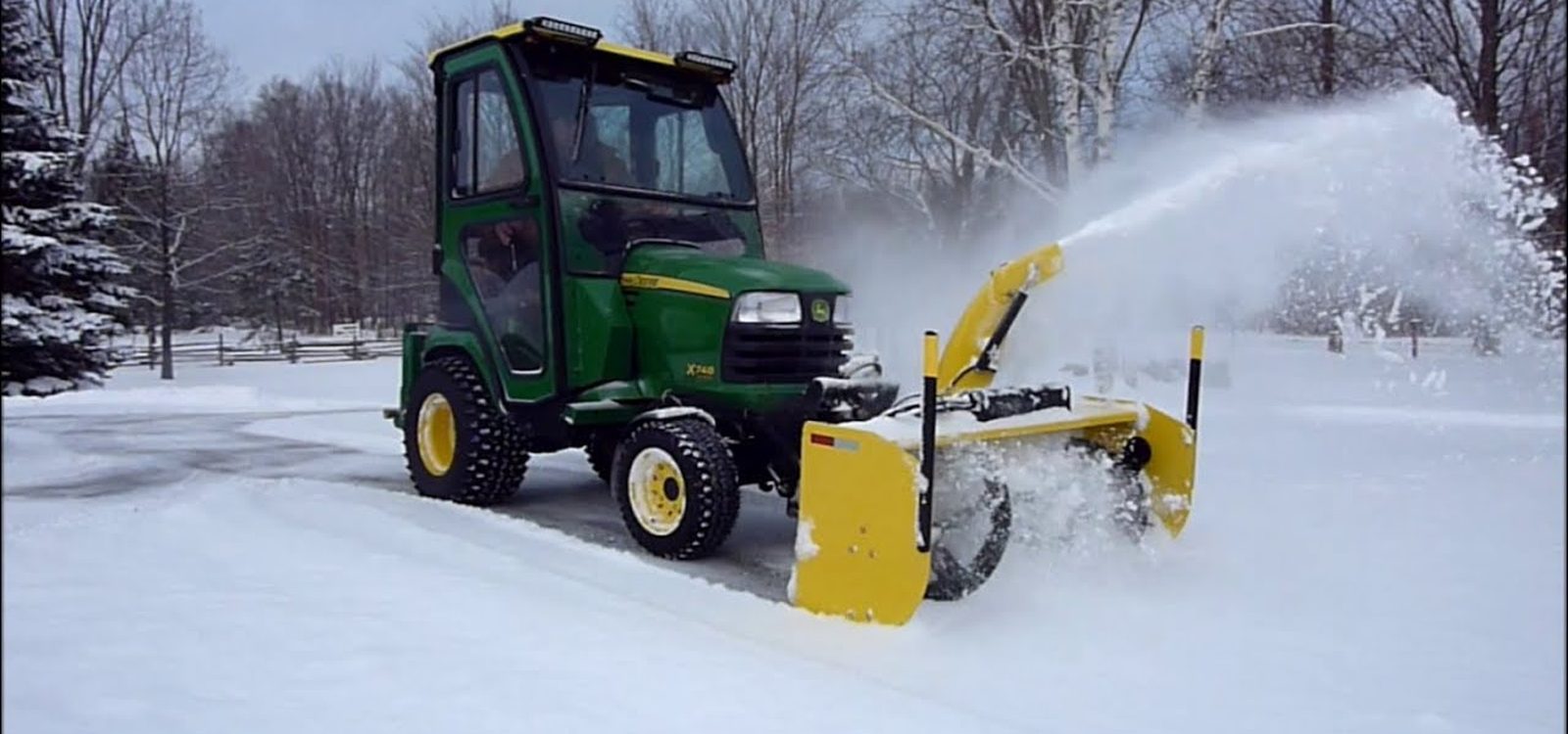 Compact tractor with a front-mounted blower throwing snow clear of a drive